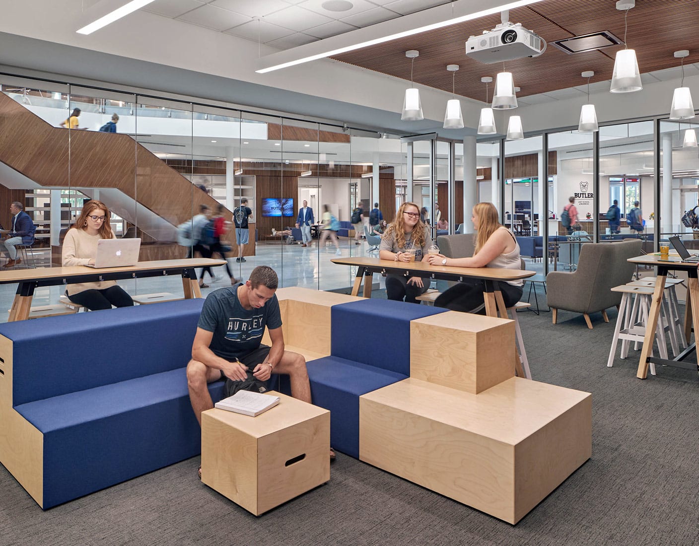 A group of individuals sitting on blue-colored and light wooden furniture in a bright, open workspace.